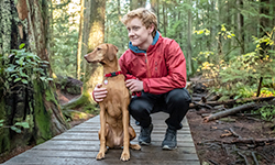 Redhead teenaged boy with Vizsla Dog resting on forest boardwalk