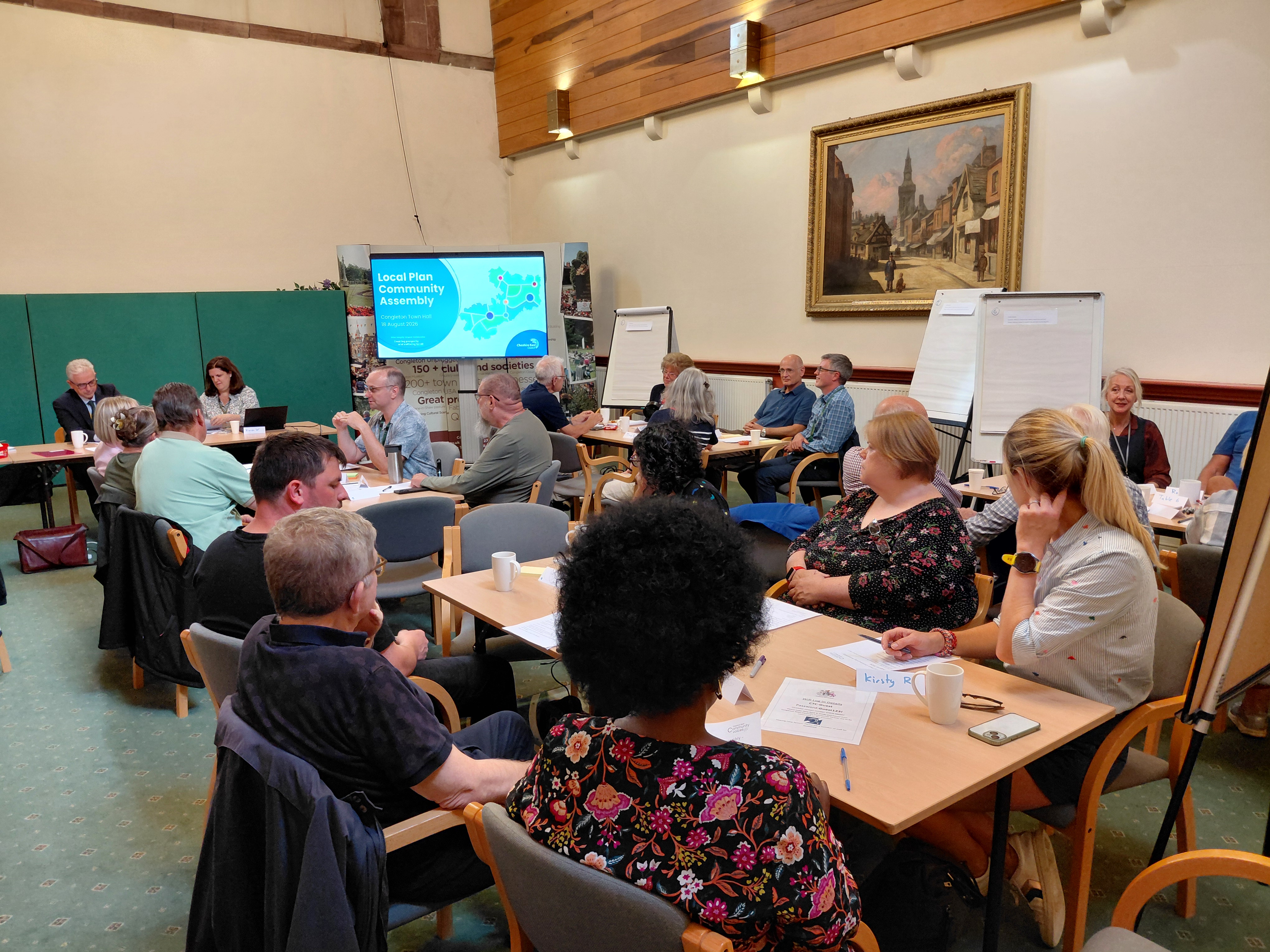 Attendees sit at several table while the main facilitators sit at the front of the event.