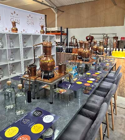 Copper gin stills and tasting benches inside The Three Wrens Gin distillery in Cheshire East, with bottles, glasses and equipment laid out.