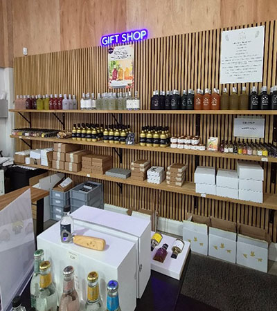 Gift shop shelves inside The Three Wrens Gin distillery in Cheshire East, displaying bottled spirits, mixers, jars and boxed gin gifts beneath a &lsquo;Gift Shop&rsquo; sign
