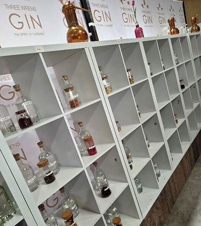 Display shelves at The Three Wrens Gin distillery in Cheshire East, showing small bottles of gin and botanicals arranged in white cubby shelves beneath branded signage.