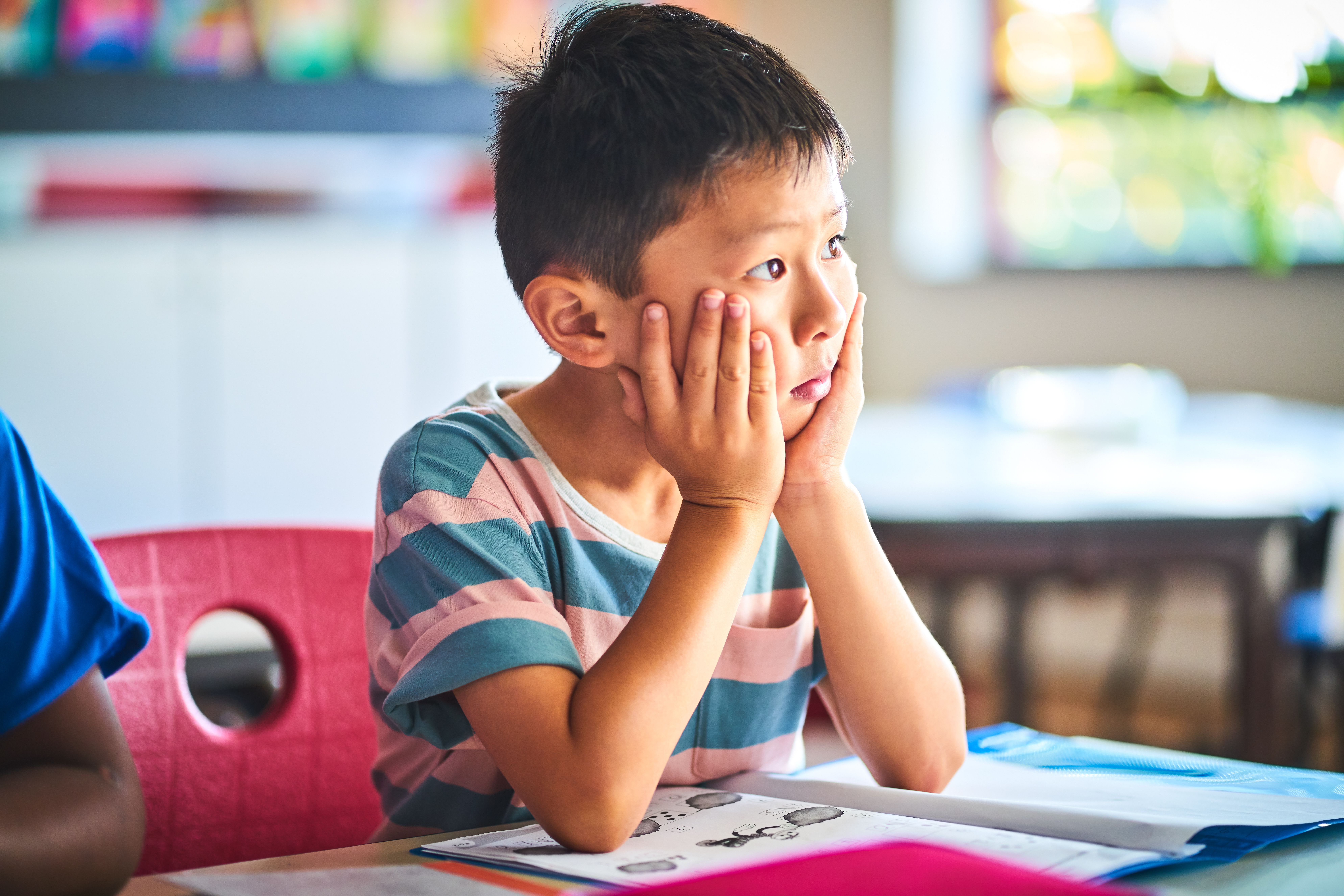 A young child sits in class with his head in his hands pondering the meaning of life.