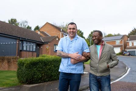 young male carer assisting a man on a walk