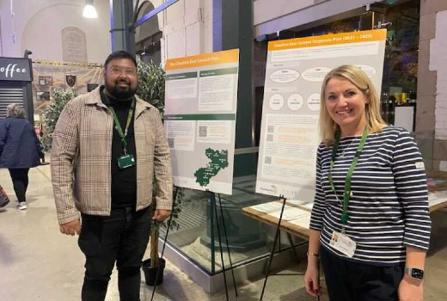 A man and a woman stood in front of some large boards explaining about an engagement activity