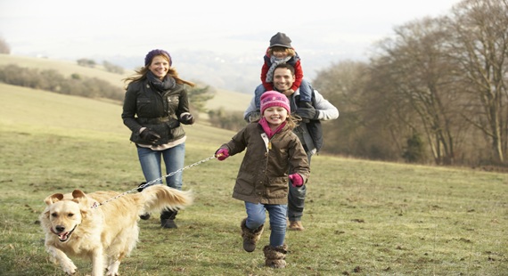 Young family walking with their dog in countryside grassland near woods in late autumn