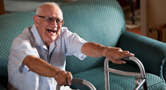 Senior man (80s) laughing, getting up from couch, using walker 570 x 310